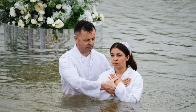 Служитель і дівчина у воді біля квіткової композиції