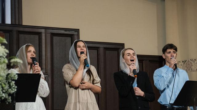 Сестри й брат співають у залі церкви
