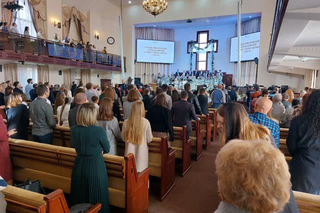 Повний зал церкви: люди стоять між лавами під час прославлення
